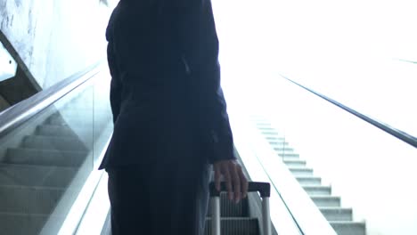 Low-angle-view-of-businesswoman-with-suitcase-on-escalator